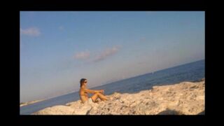 A young girl is basking in the sun naked on the beach