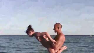 A group of naked gymnasts are doing acrobatic exercises on the beach